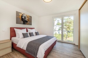 Ein Schlafzimmer mit einem Bett, einem Nachttisch, einem Gemälde und einem großen Fenster.
