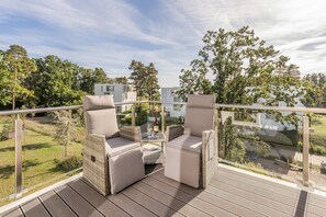 Eine Terrasse im Freien mit Korbmöbeln und einer Glasreling mit Blick auf eine grüne Landschaft.