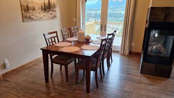 A dining area with a wooden table, chairs, placemats, and a view of a mountainous landscape through a glass door.