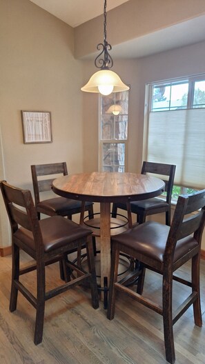 Una mesa de comedor redonda de madera con cuatro sillas, una lámpara colgante y una ventana con persianas.
