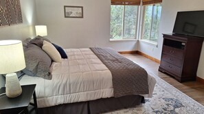 Un dormitorio con cama, lámparas de noche, cómoda y ventana con vista a árboles.