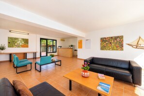 A spacious living area with a black leather sofa, teal chairs, a wooden coffee table with a vase, and a kitchen in the background. - Nireas Studios and Apartments (Acharavi)