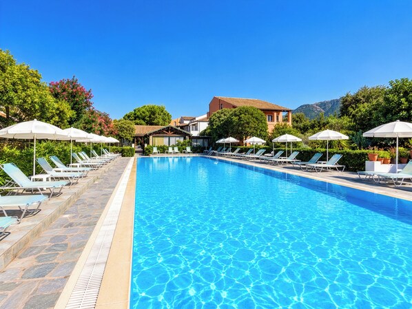 A clear blue swimming pool with lounge chairs and umbrellas, surrounded by greenery and buildings. - Nireas Studios and Apartments (Acharavi)