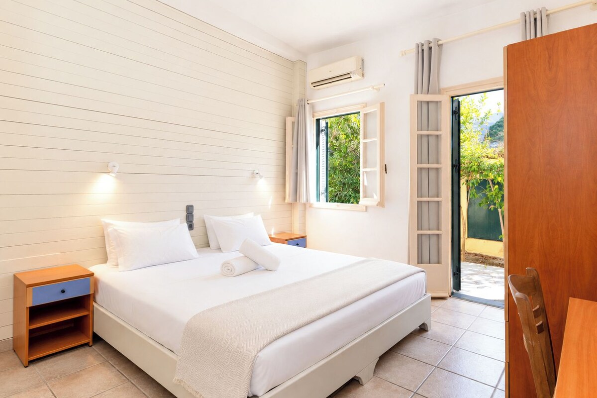 A hotel room with a bed, bedside tables, a window, and an air conditioning unit.