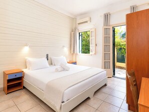 A hotel room with a bed, bedside tables, a window, and an air conditioning unit. - Nireas Studios and Apartments (Acharavi)