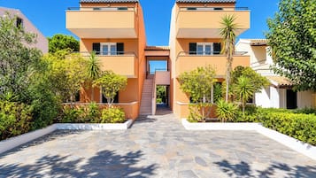 Um edifício moderno com uma escadaria central, cercado por vegetação bem cuidada e um calçadão pavimentado.
