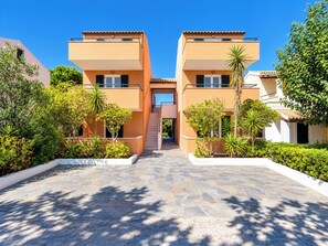 A modern building with a central staircase, surrounded by well-maintained greenery and a paved walkway. - Nireas Studios and Apartments (Acharavi)