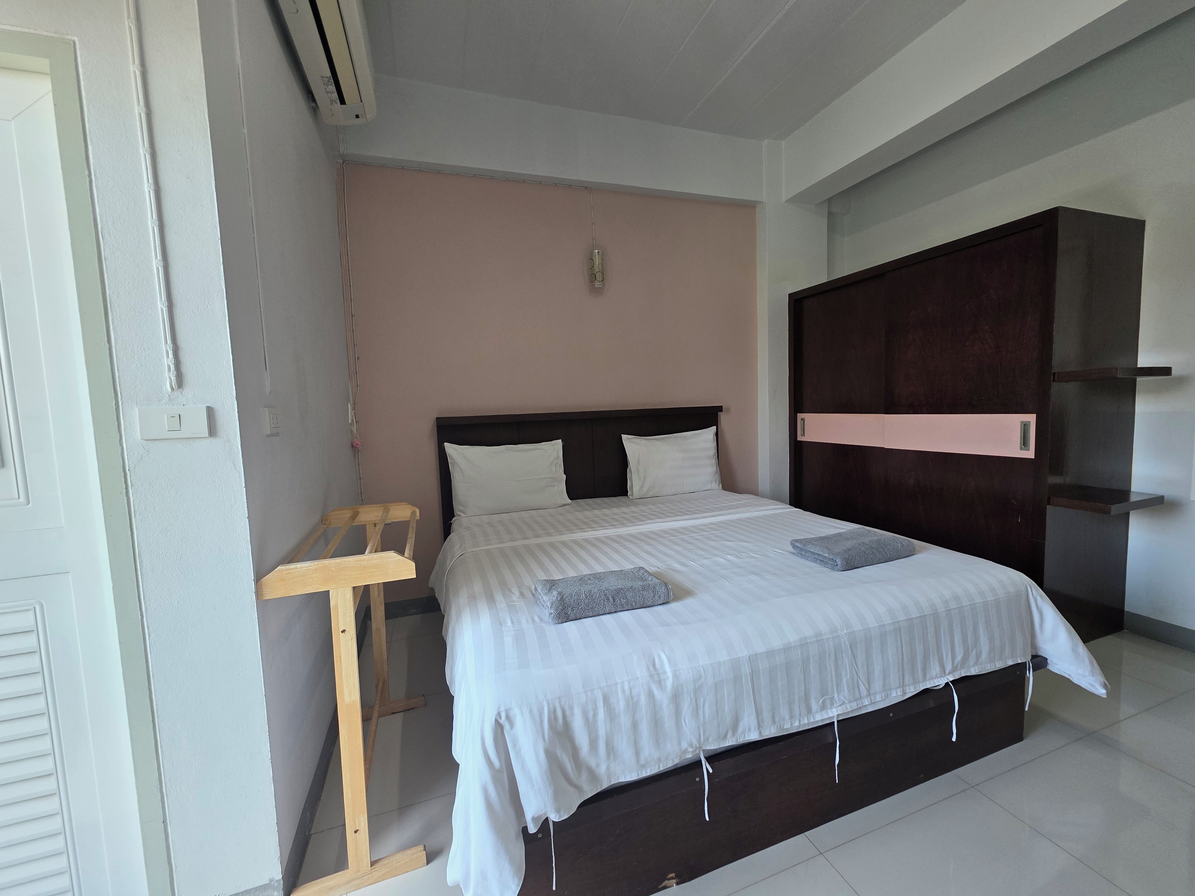 A hotel room with a bed, a wooden chair, a wardrobe, and a wall-mounted shelf.
