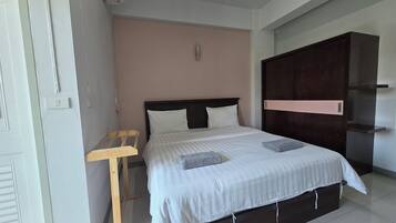 A hotel room with a bed, a wooden chair, a wardrobe, and a wall-mounted shelf.