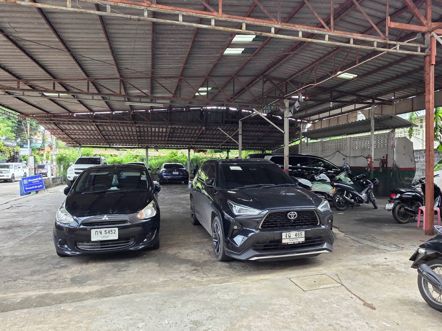 A covered parking area with two cars and several motorcycles.