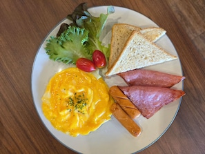 Un plato con huevos revueltos, jamón, salchichas, lechuga, tomates cherry y tostadas.