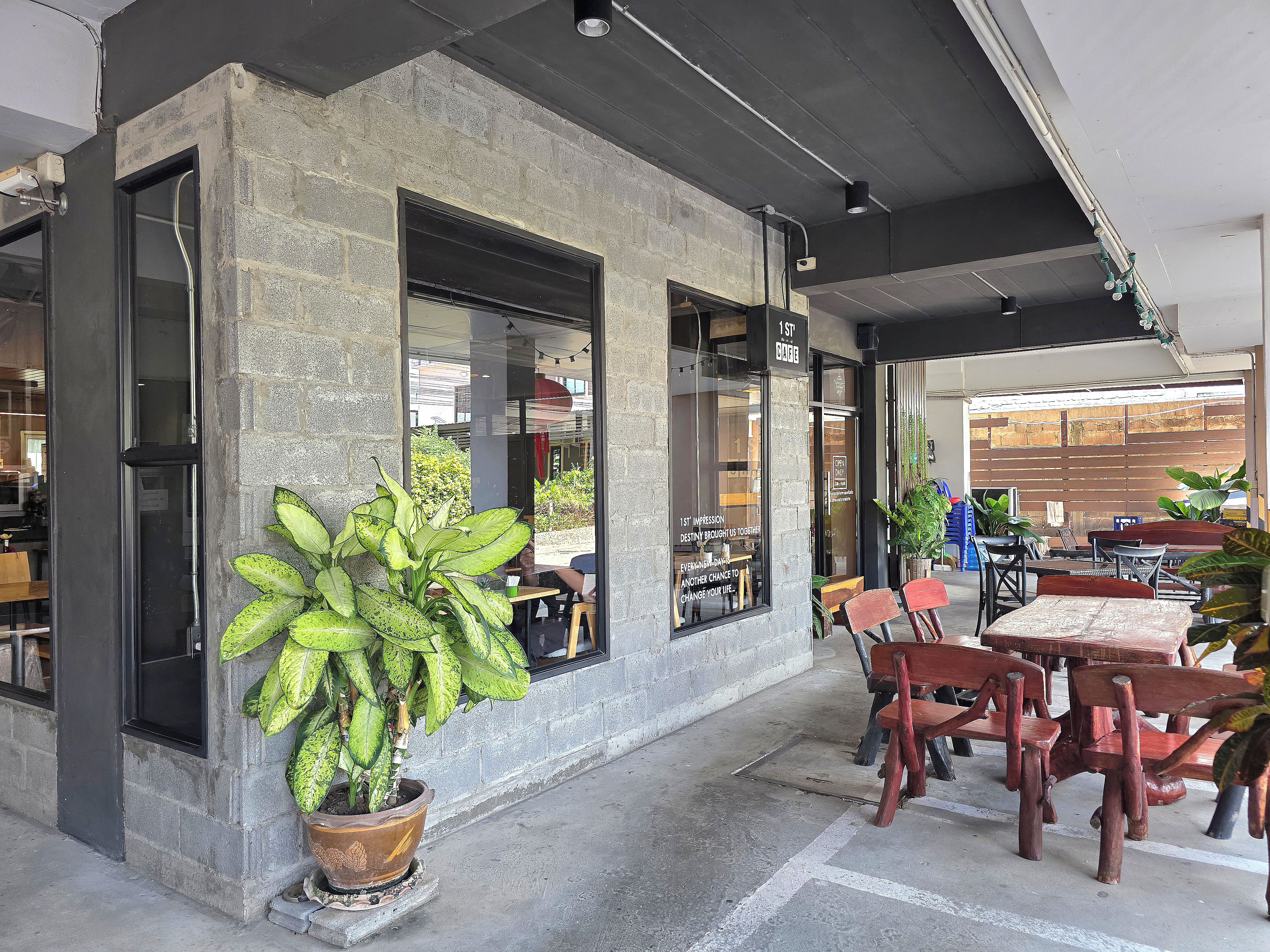 A cafe with outdoor seating, a large potted plant, and a brick wall.