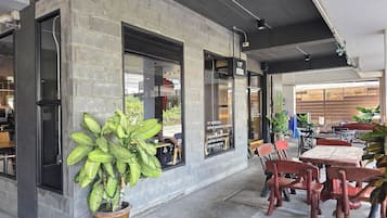 A cafe with outdoor seating, a large potted plant, and a brick wall.