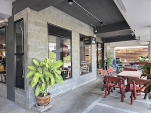 A cafe with outdoor seating, a large potted plant, and a brick wall. - Jiranakron Park (Mueang Buriram)