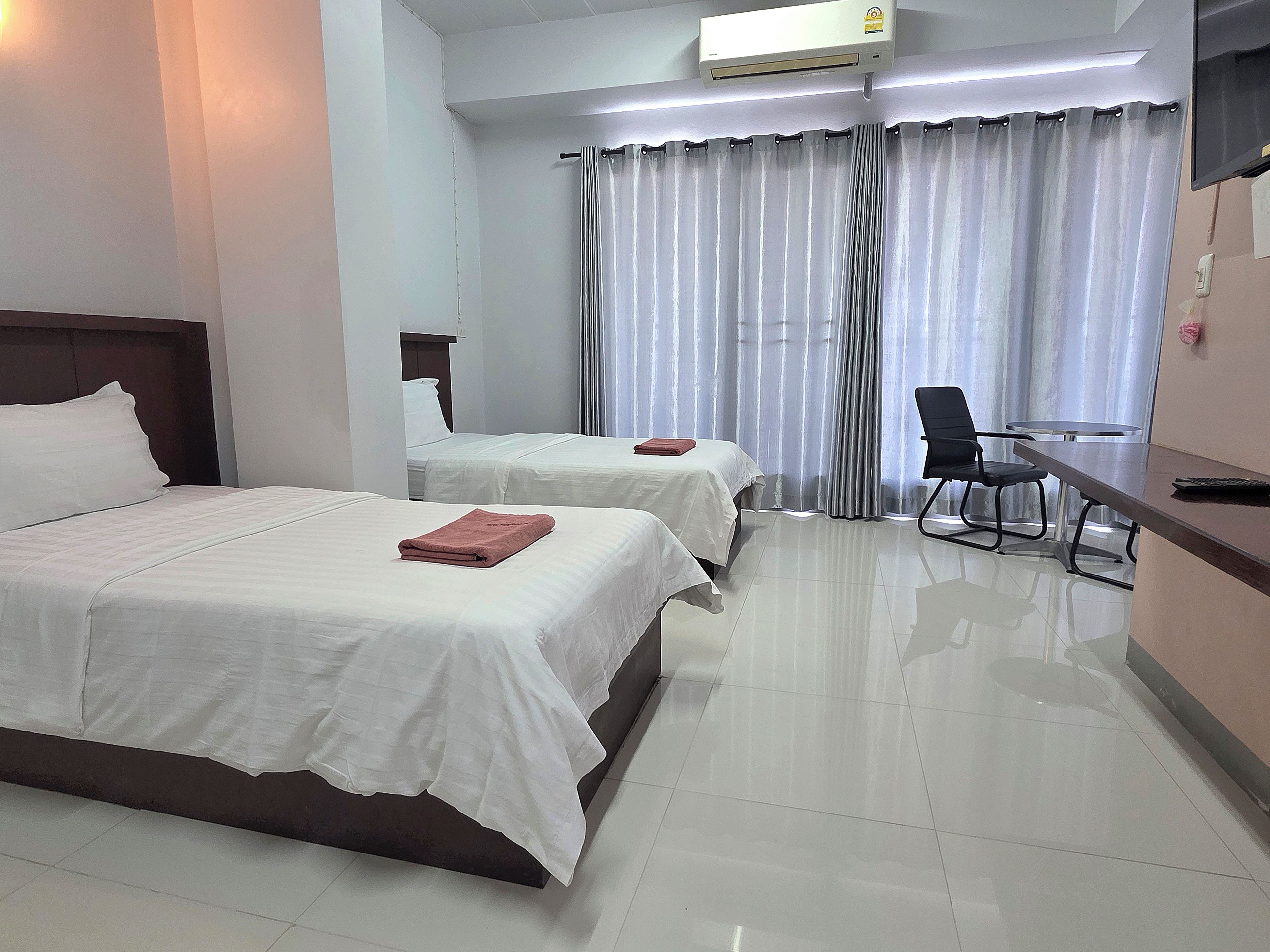 A hotel room with two beds, a desk, a chair, and a TV.