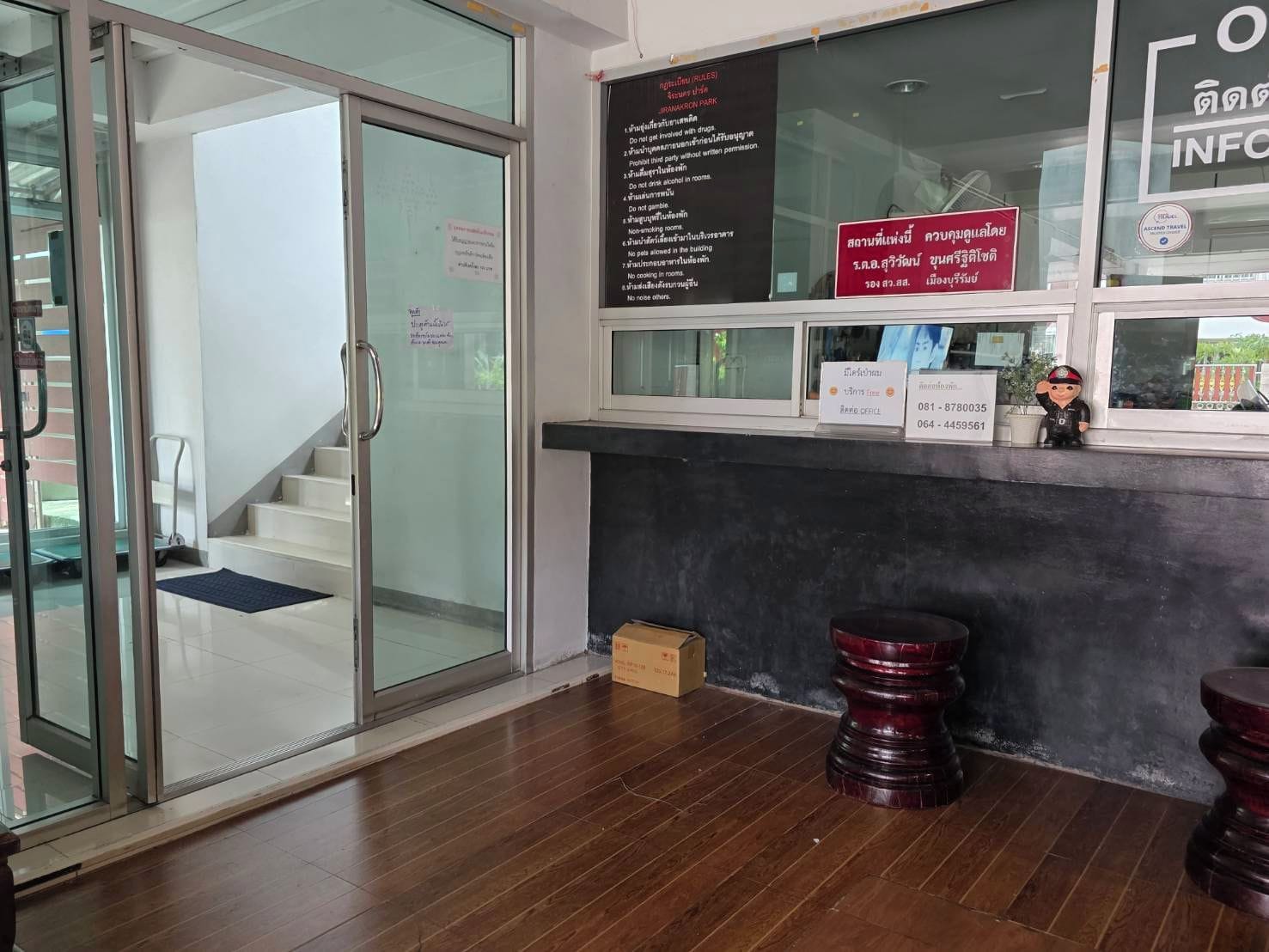 Zona de recepción con entrada por puerta de cristal, suelo de madera, un pequeño escritorio con teléfono y un tablón informativo en la pared.