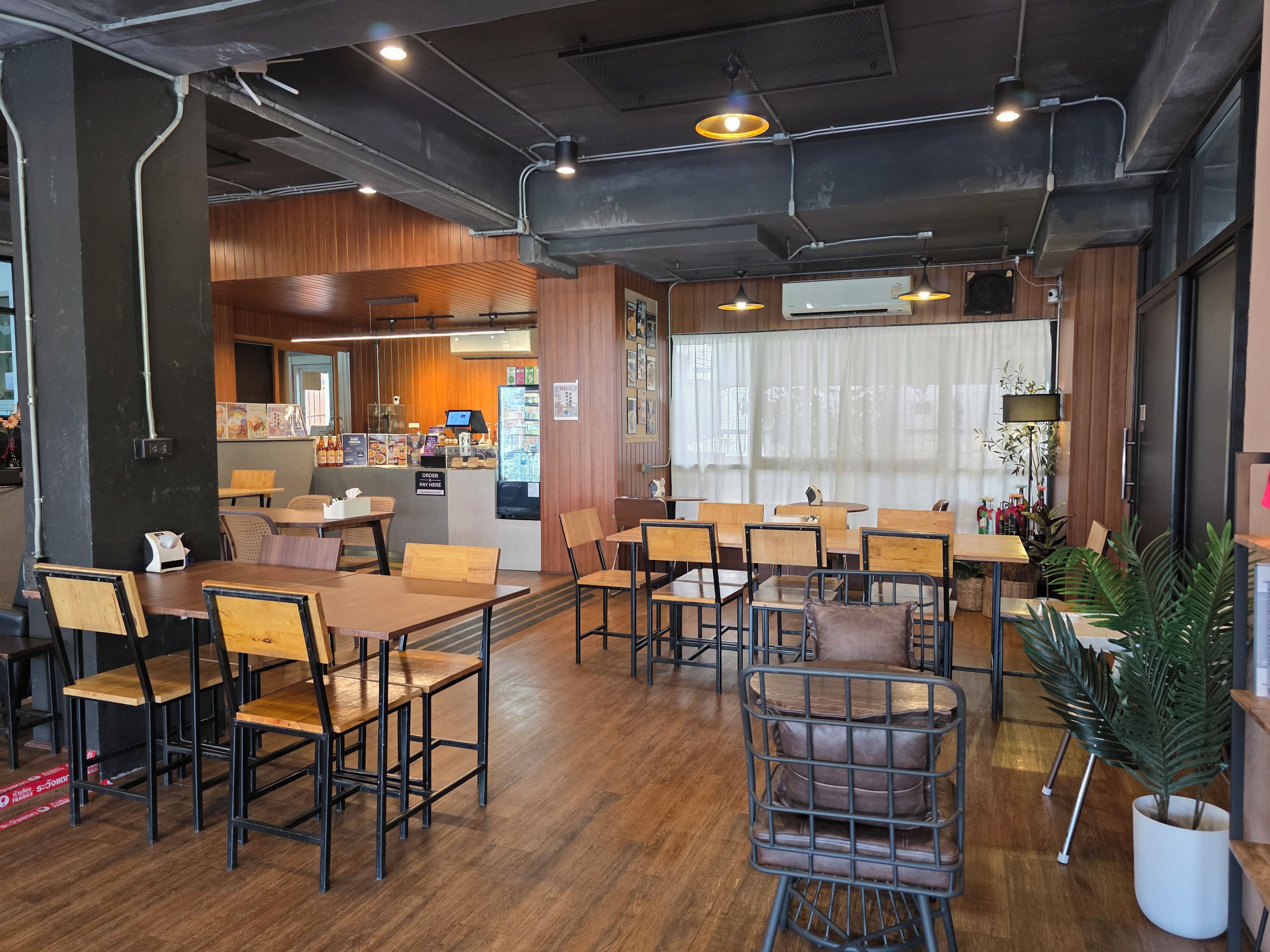 A restaurant interior with wooden tables and chairs, a counter with a menu, and an air conditioning unit on the wall.