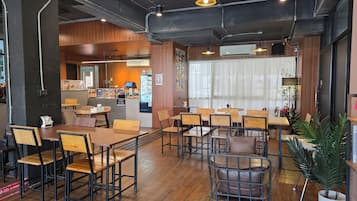 A restaurant interior with wooden tables and chairs, a counter with a menu, and an air conditioning unit on the wall.