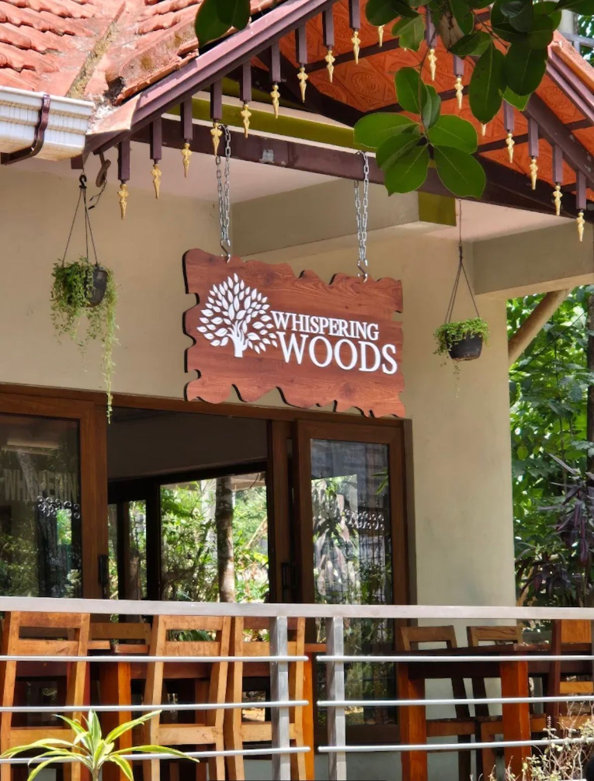 Un letrero de madera con el texto 'Whispering Woods' colgando sobre la barandilla de un balcón de madera.