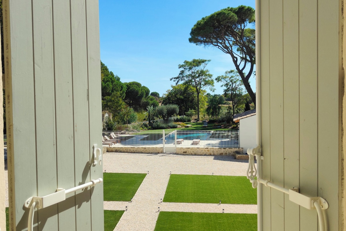 A view through open doors to a pool area with a clear sky, a tree, and a gravel path.