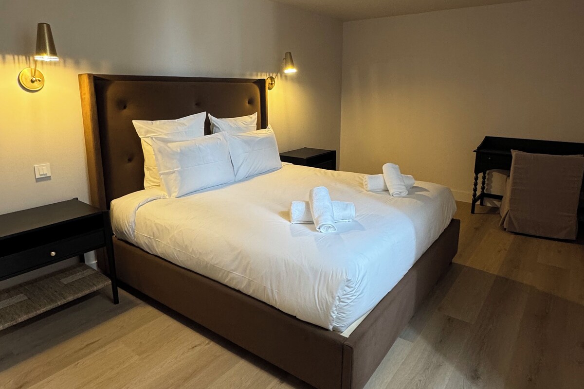 A neatly made bed with white linens and towels, a dark headboard, and two bedside lamps.