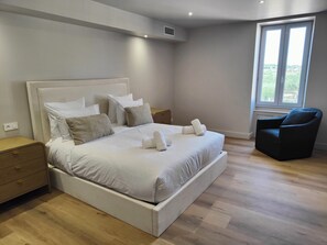 A modern bedroom with a large bed, a nightstand, a chair, and a window with a view. - Domaine de Grange Basse (Vendres)