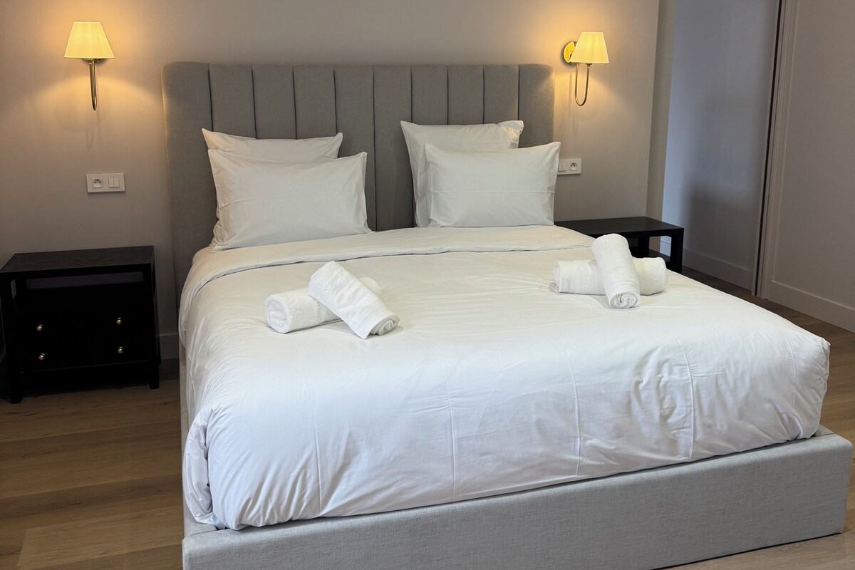 A double bed with white linens, two bedside tables with lamps, and a grey headboard.
