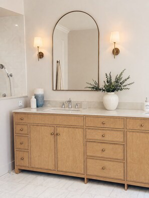 A bathroom with a wooden vanity, a large mirror, two wall-mounted lights, a shower, and a potted plant. - Domaine de Grange Basse (Vendres)
