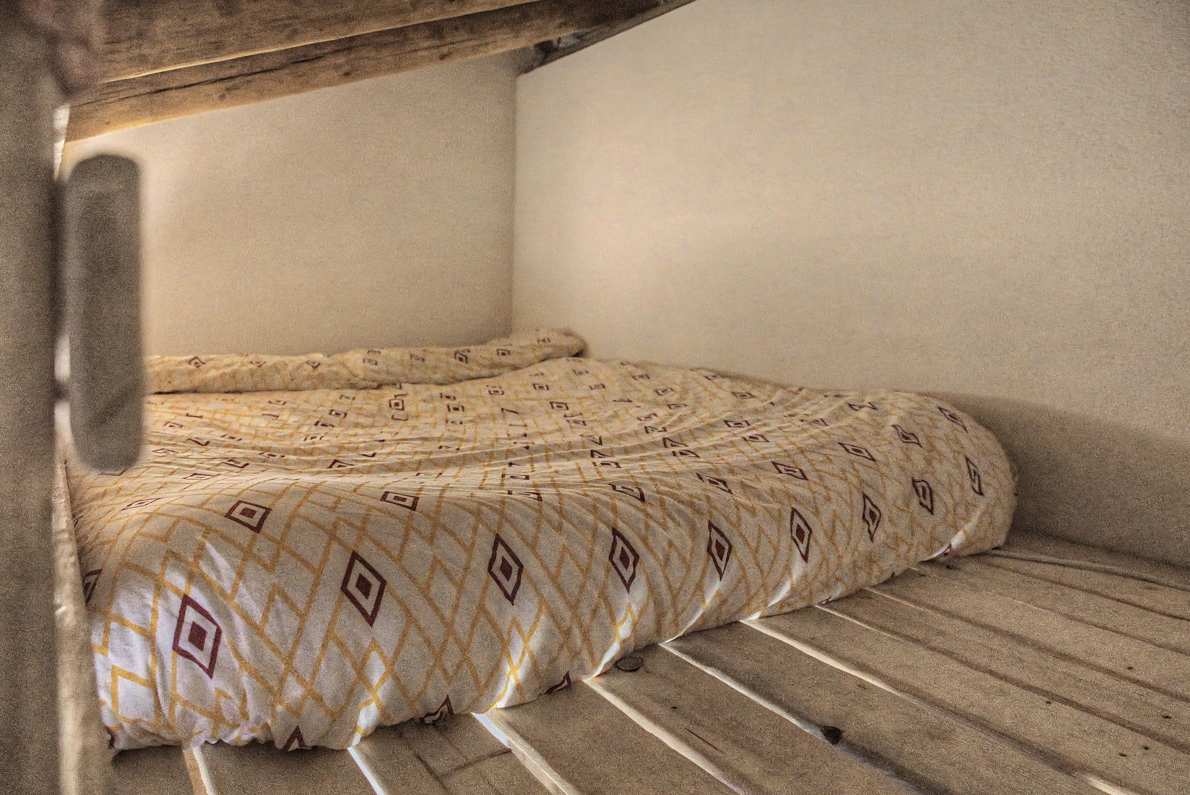 A corner bedroom with a bed, a wooden headboard, and a patterned bedspread.
