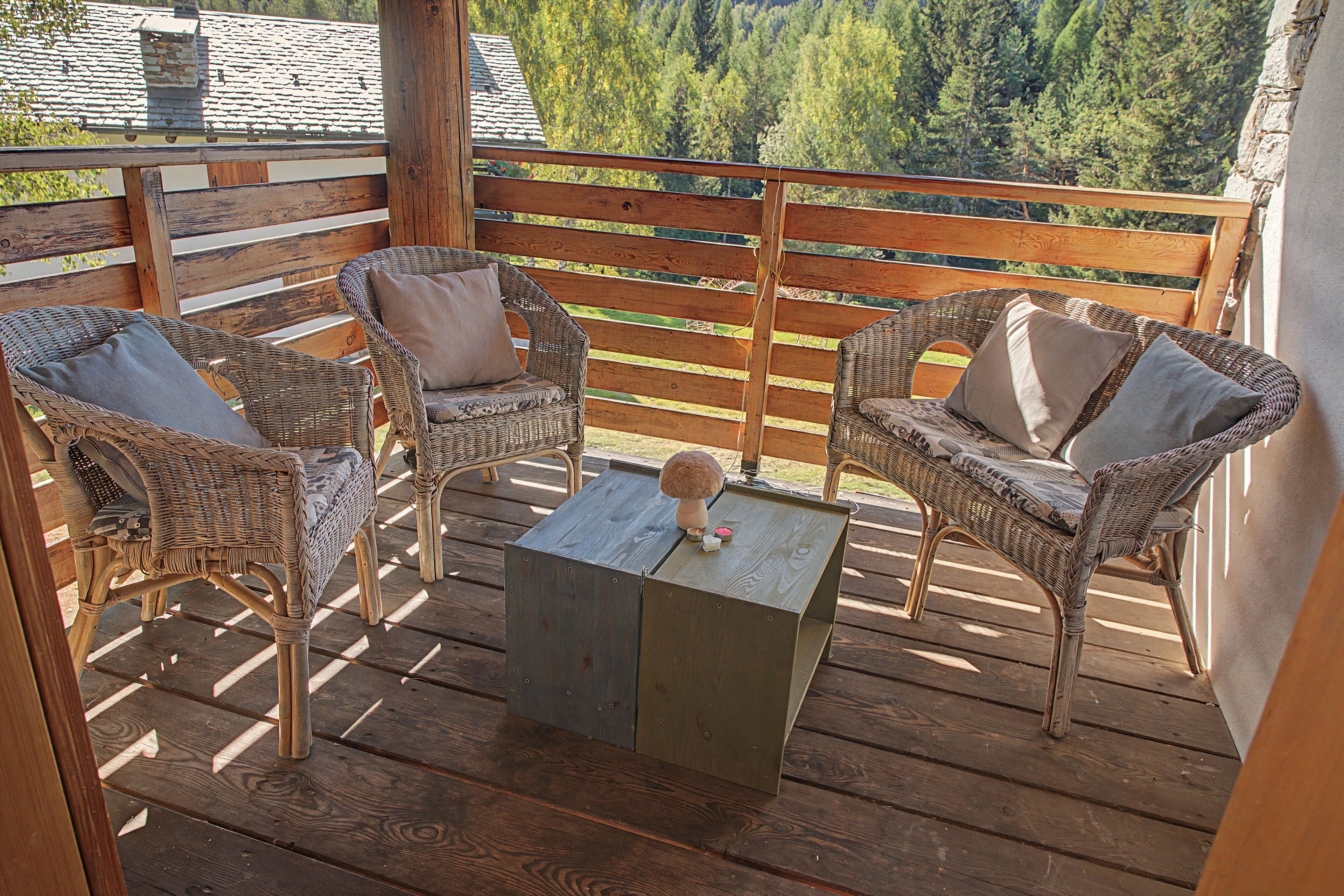 Eine Holzterrasse mit Korbstühlen und einem Tisch, mit Blick auf eine bewaldete Landschaft.