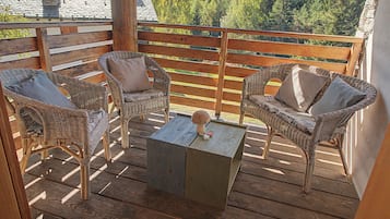 Eine Holzterrasse mit Korbstühlen und einem Tisch, mit Blick auf eine bewaldete Landschaft.