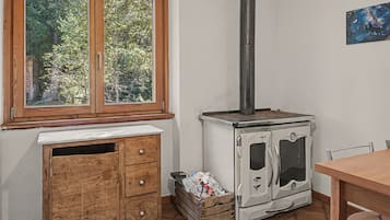 Eine Küche mit Holzofen, einem Fenster mit Blick auf Grünflächen und einem Holzkabinett.