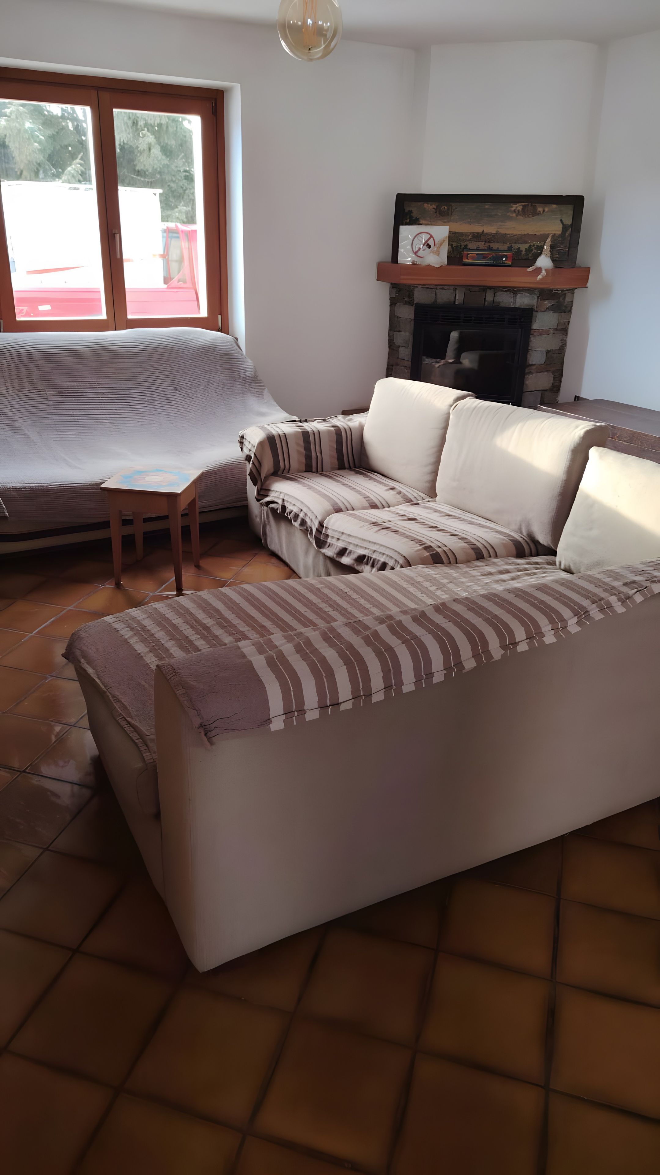 Een woonkamer met een bank, een open haard en een raam met uitzicht op bomen.