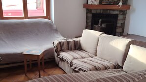 Ein Wohnzimmer mit einer Couch, einem Kamin und einem Fenster mit Blick auf Bäume.