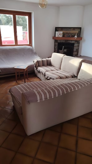 Ein Wohnzimmer mit einer Couch, einem Kamin und einem Fenster mit Blick auf Bäume.