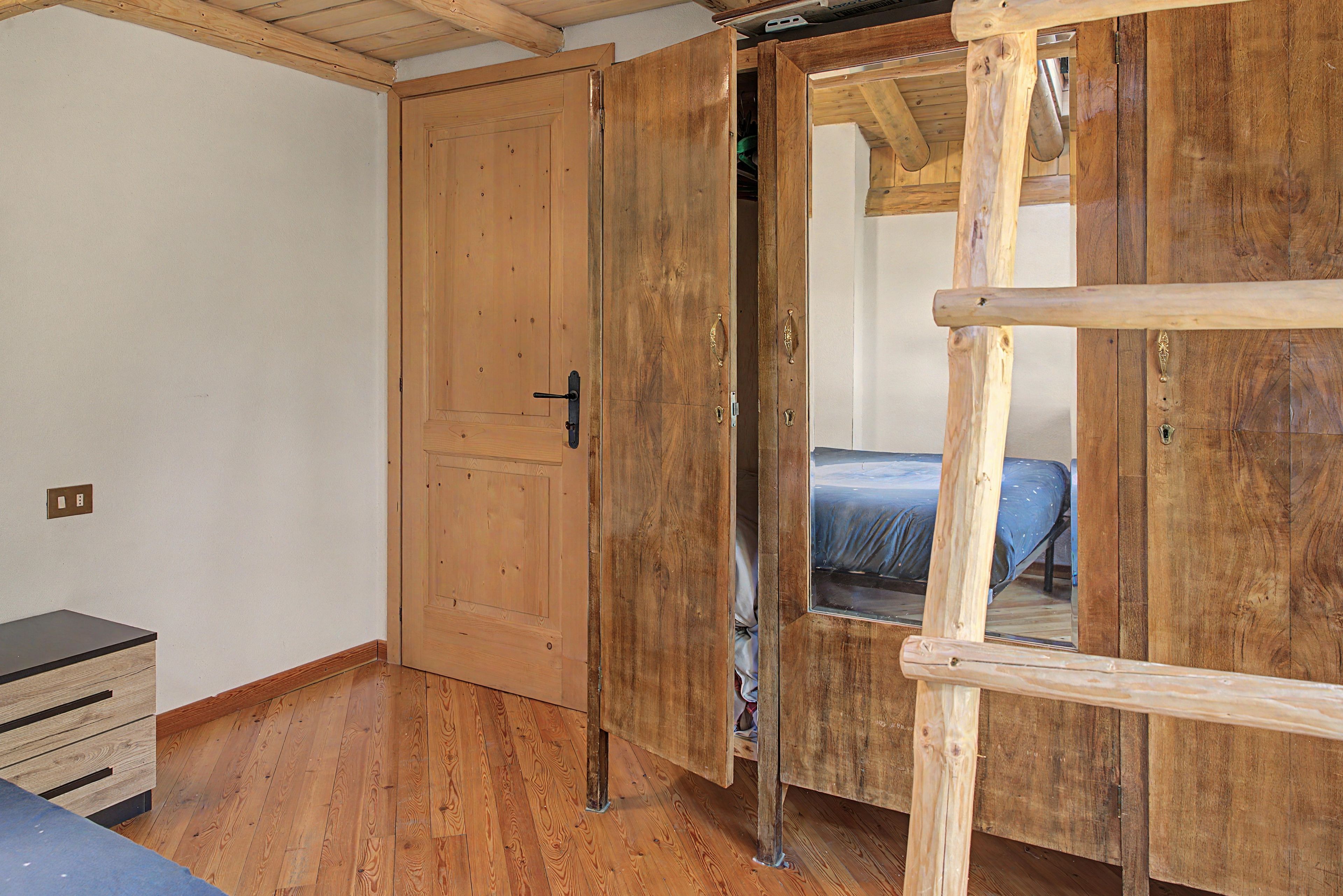 Ein Zimmer mit Holztür, einem Bett mit blauer Matratze und einem kleinen Holzschrank.
