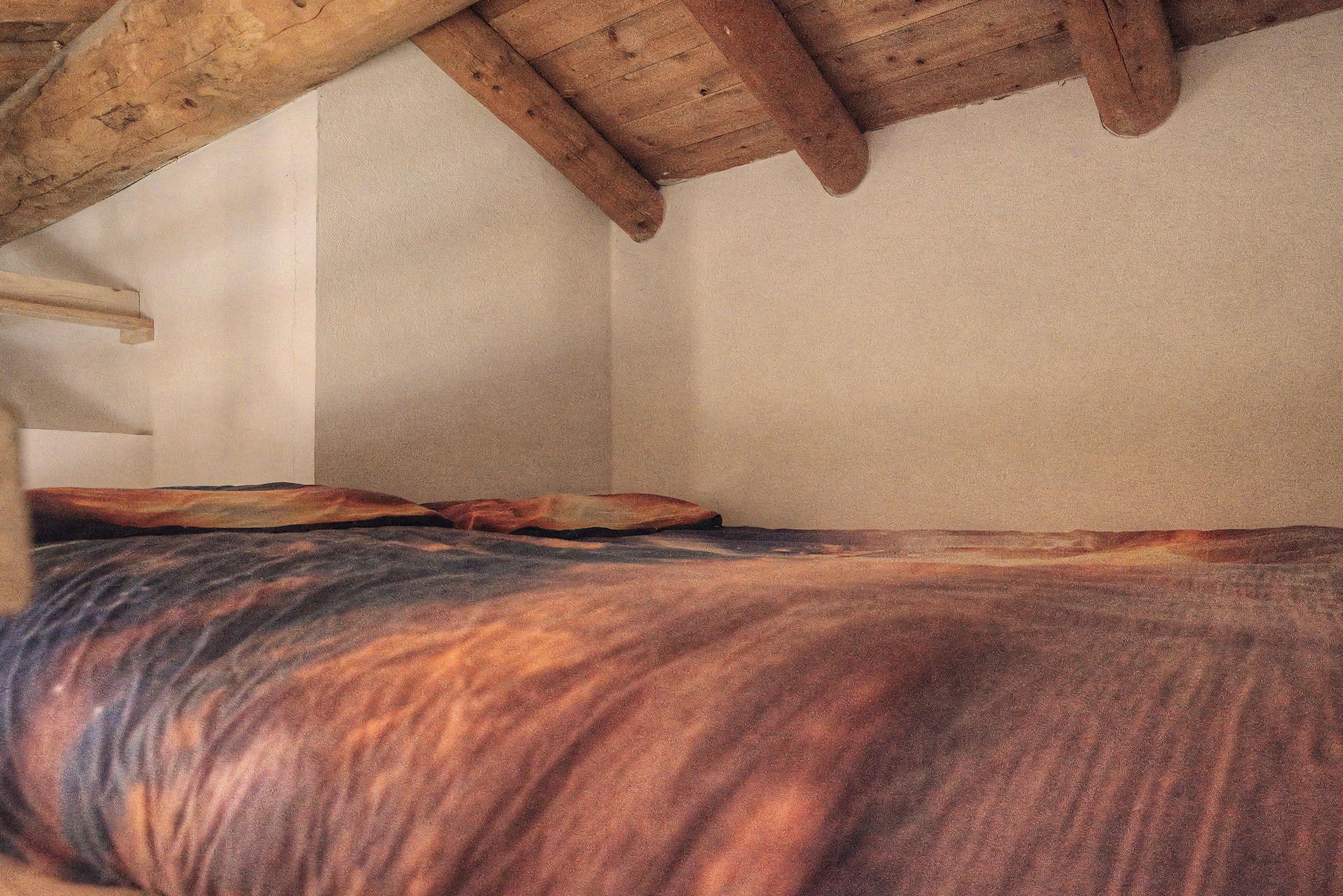 Een kamer met een bed, een houten plafond en een effen muur.