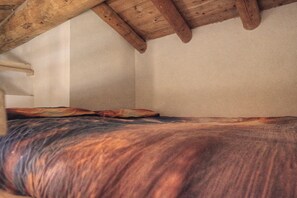 A room with a bed, a wooden ceiling, and a plain wall.