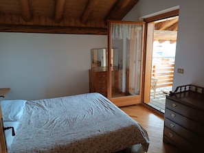 Ein Schlafzimmer mit einem Bett, einem Holzkapmierer, einem Spiegel und einer Glastür zum Außenbereich.