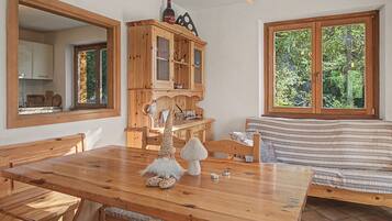 A wooden dining table with benches, a wooden cabinet with glass doors, a gnome decoration, and a window with a view of trees.