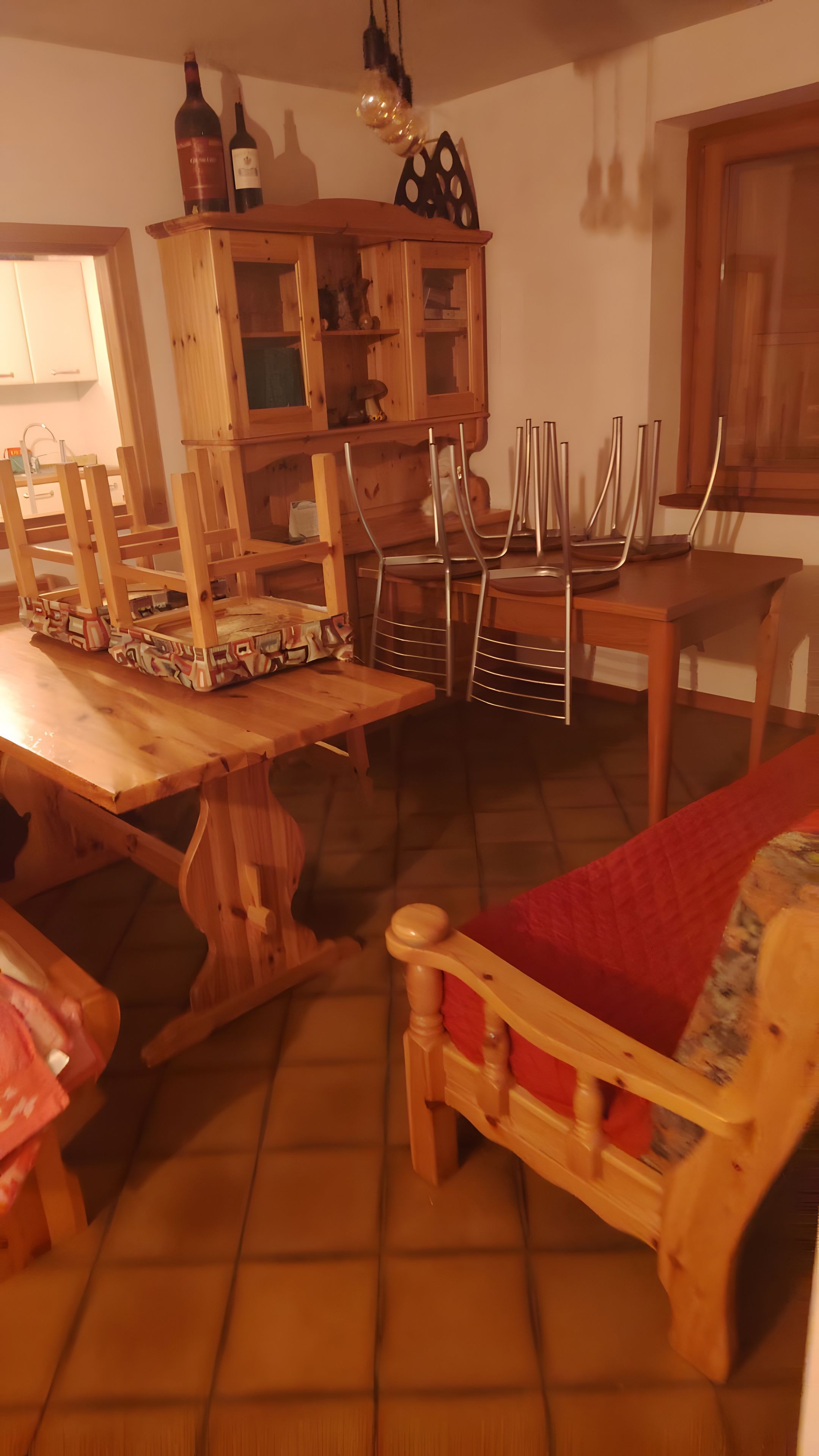 Een eetgedeelte met een houten tafel, stoelen en een kast met wijnflessen.