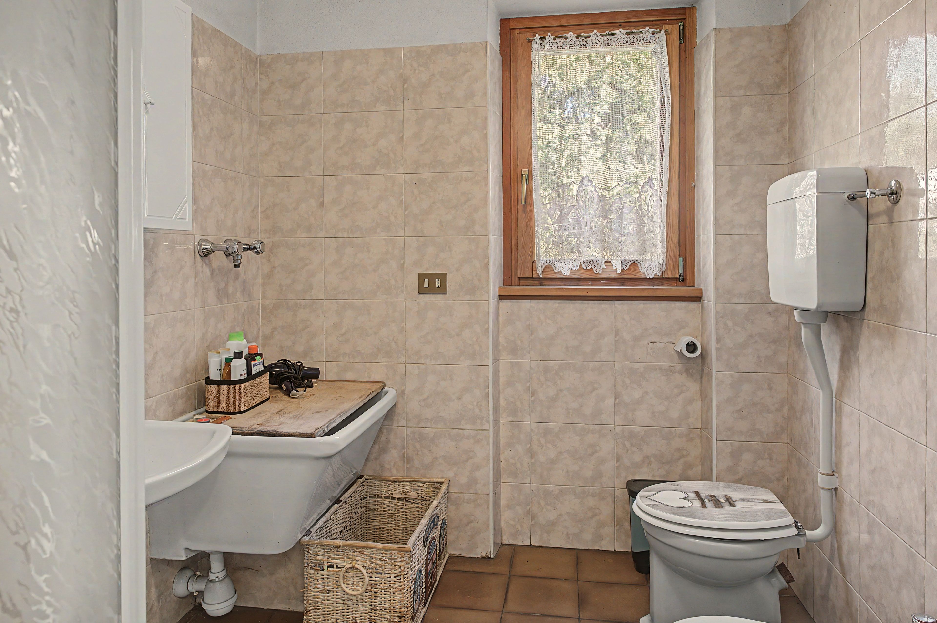 A bathroom with a toilet, sink, and window with lace curtain.
