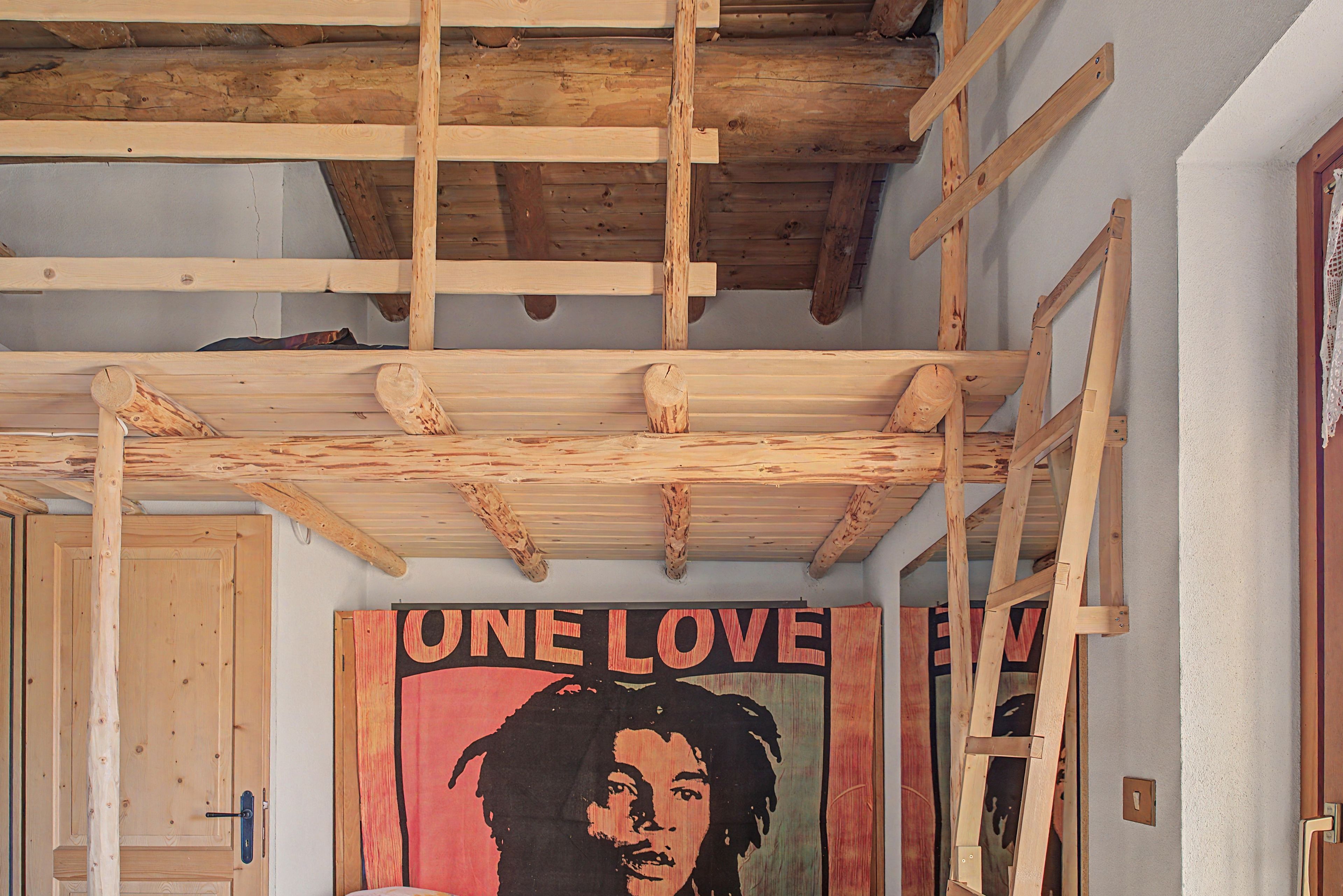 Et værelse med synlige træbjælker, en dør og et plakat med teksten 'ONE LOVE' på væggen.
