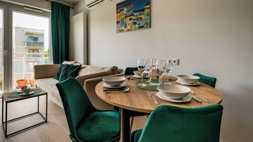 Un comedor moderno con una mesa redonda de madera, sillas tapizadas en verde y vistas a un balcón con un paisaje urbano.