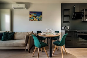 A modern living room with a sofa, dining table, and chairs, a kitchen with cabinets and appliances, and a painting on the wall. - RentPlanet - Apartament Wichrowa (Wrocław)