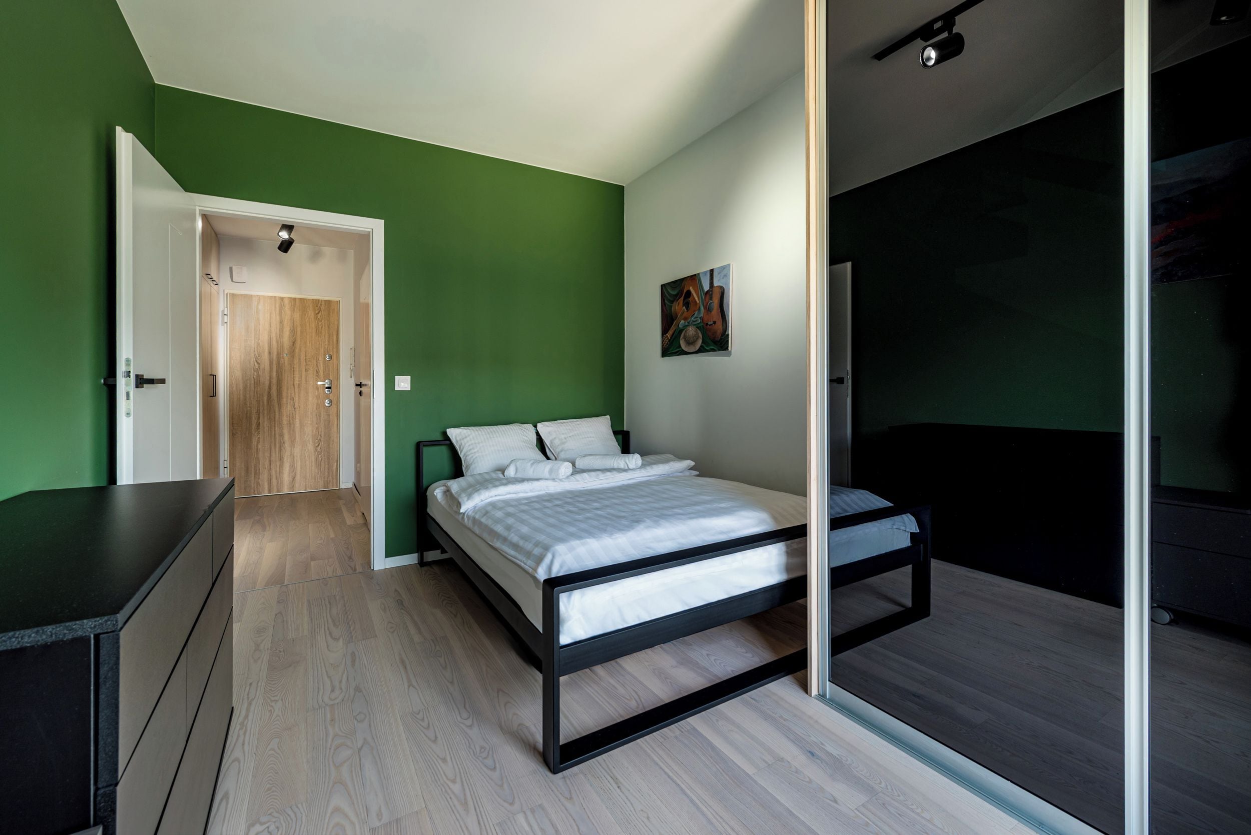 Une chambre à coucher avec un lit, une commode, une porte et un tableau au mur.