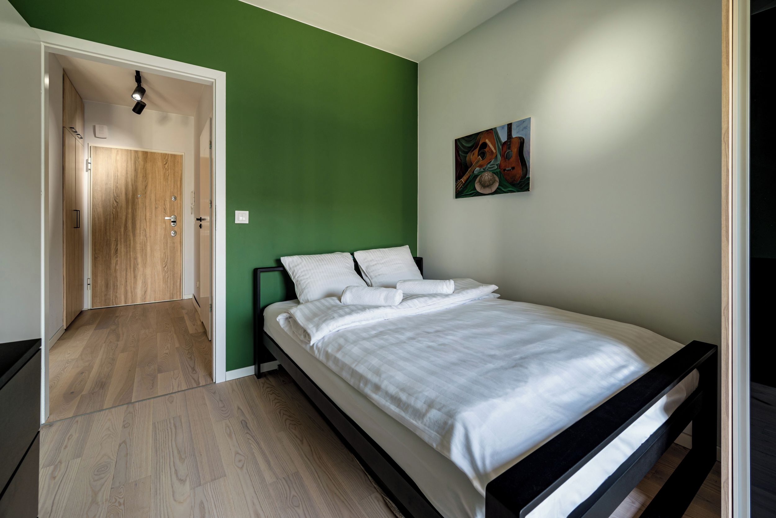 Un dormitorio con una cama, una pared verde y una puerta que da a otra habitación.