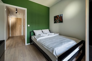 A bedroom with a bed, a green wall, and a door leading to another room. - RentPlanet - Apartament Wichrowa (Wrocław)