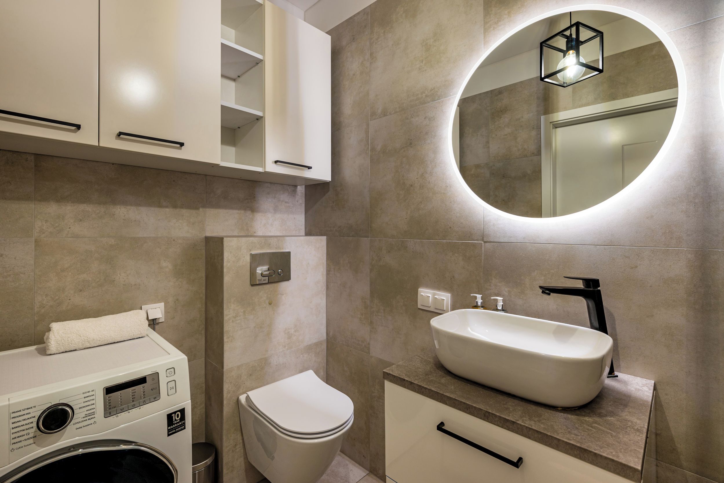 A modern bathroom with a built-in washing machine, a toilet, and a sink with a mirror above.