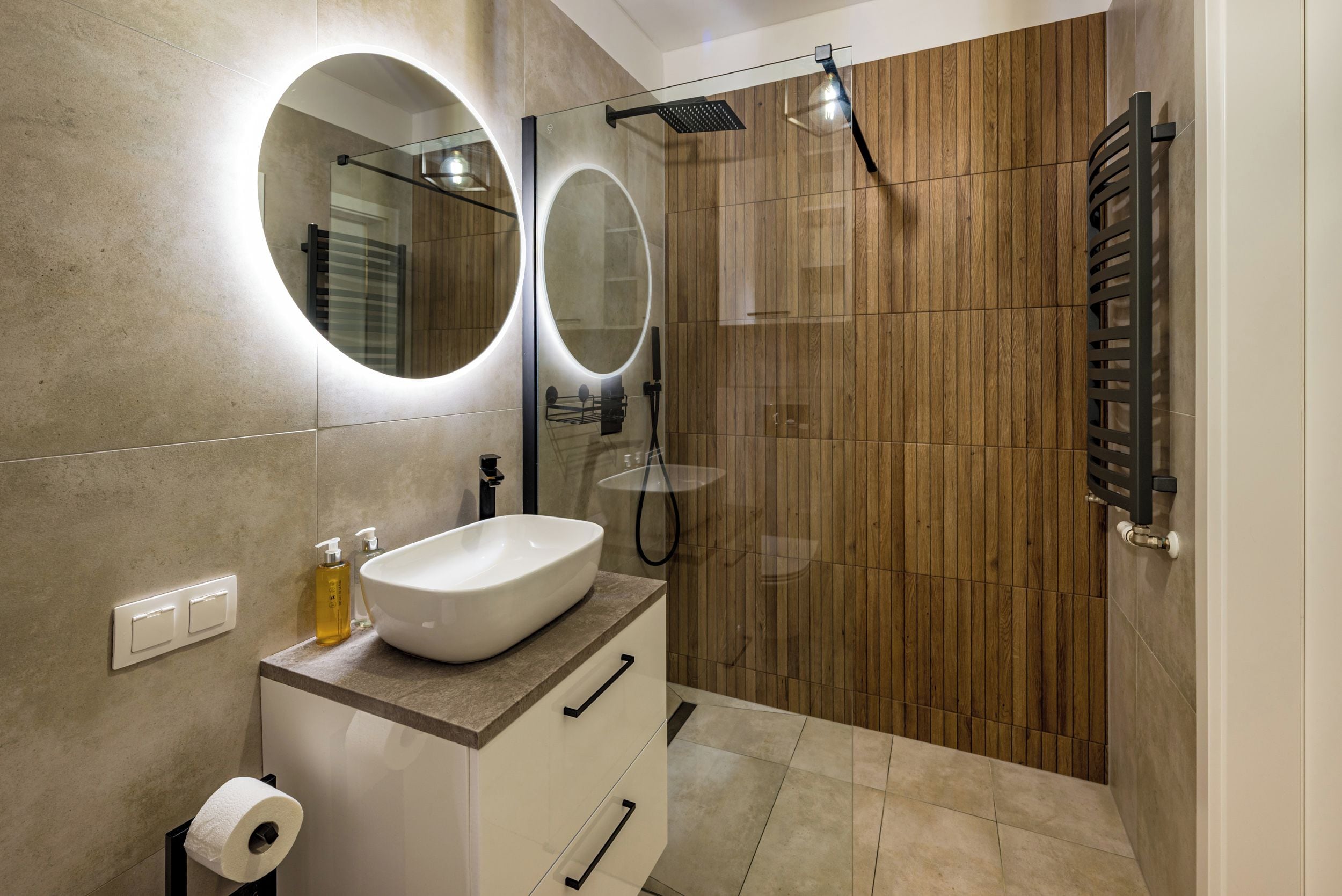 A modern bathroom with a large oval mirror, a white sink, and a glass shower enclosure.